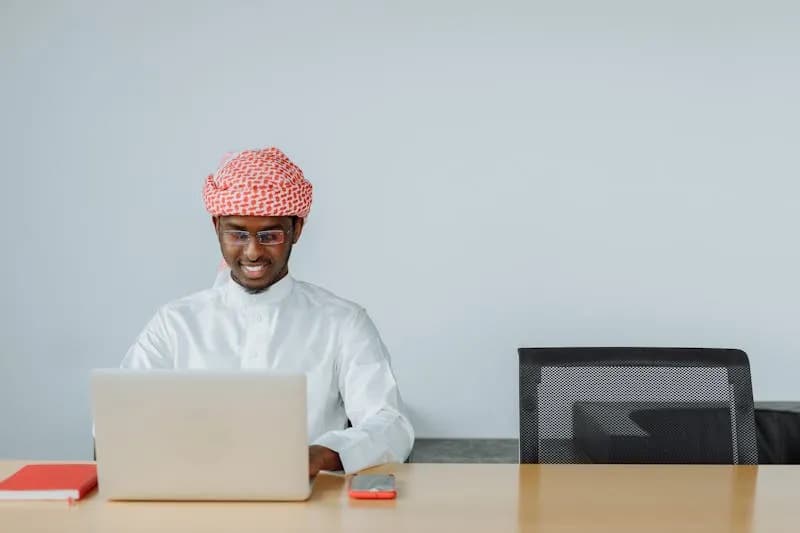 Saudi businessman in traditional attire working on laptop in modern office