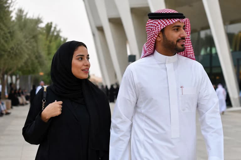 Man in white thobe with red ghutra headscarf, woman in flowing black abaya