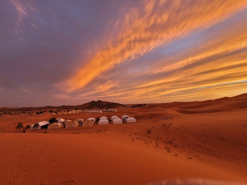 Desert camp tents at sunset among sand dunes