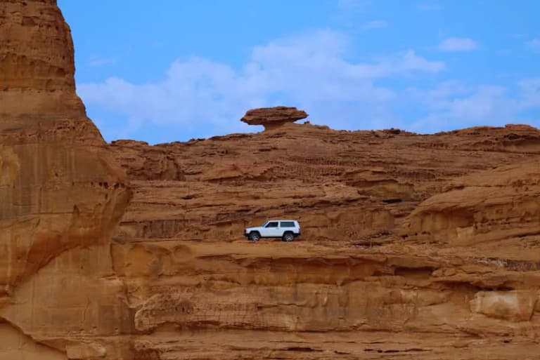 SUV driving through dramatic sandstone cliffs in AlUla