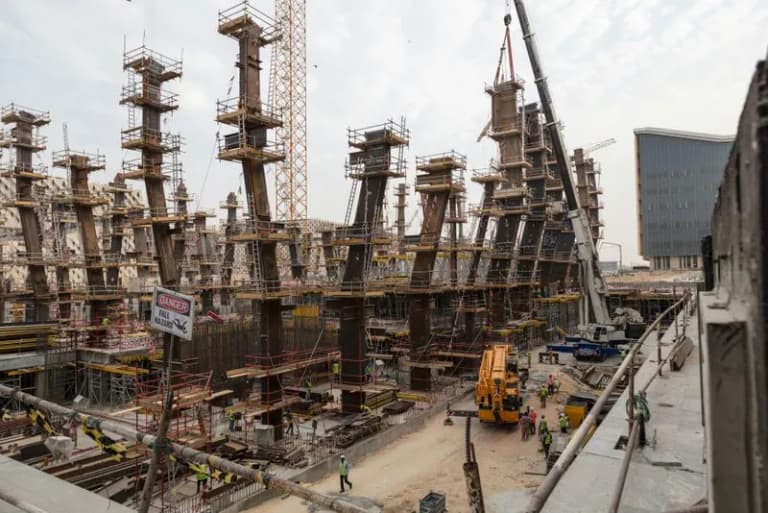 A large construction site with steel frameworks and cranes under a clear sky