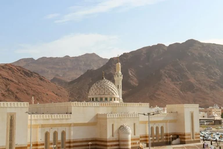 A mosque in Medina set against the backdrop of the Uhud mountains under a clear blue sky